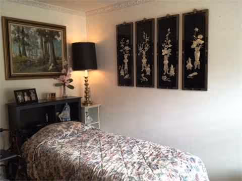 A single bed with floral quilt in a small, well-lit bedroom with wall decor.
