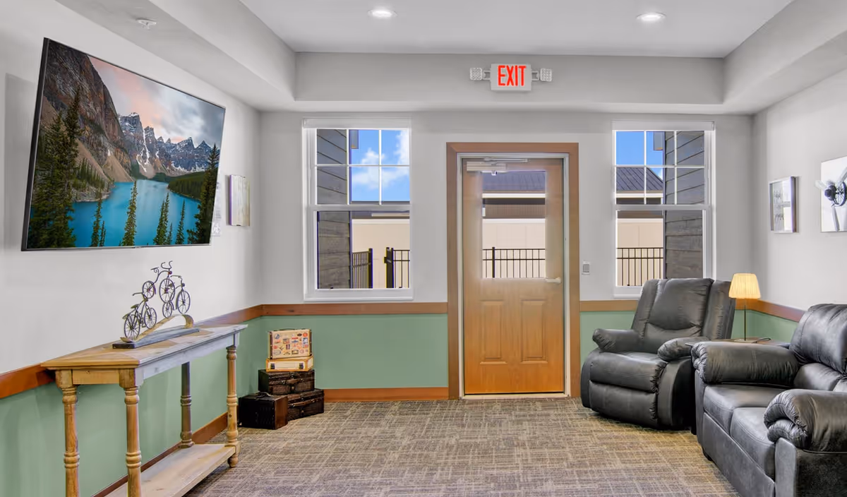 Well-lit seating area with leather recliners, a wall-mounted TV, console table and a central door with side windows.
