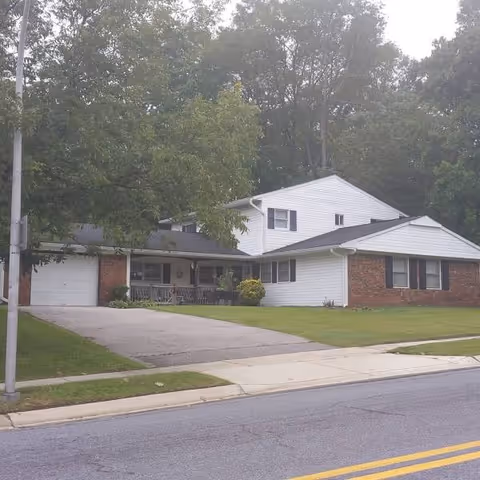 Front exterior of a single-story brick/white assisted living home with driveway.