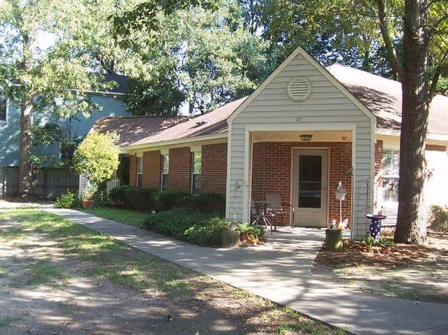 A single-story brick senior living building with a small front porch, walkway, and surrounding trees.