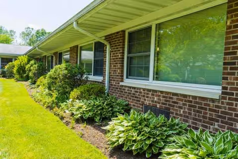 Brick exterior of a senior living facility with landscaped shrubs along the wall.