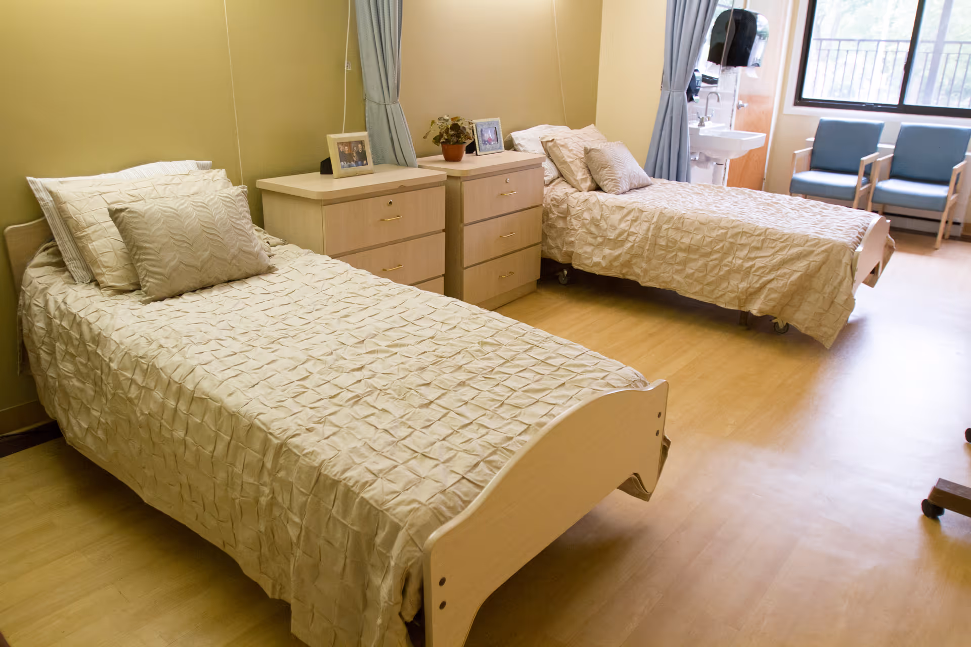 A bright shared bedroom with two single beds, dressers between them, a sink by the window and chairs.