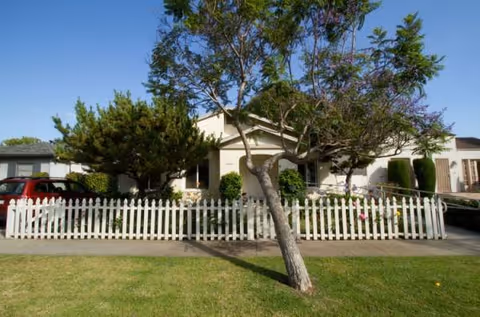 Single-story residential care home with white picket fence and small front yard.