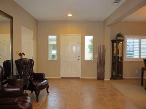Spacious foyer with tiled floor, front door, chairs, and display cabinet in a senior residence.