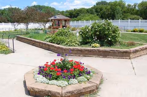 Outdoor courtyard with circular flower beds, a gazebo, and a white fence in the background.
