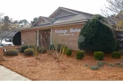 Exterior view of a single-story brick building with a sign that reads Heritage Home of Florence Inc. The building is surrounded by landscaped bushes and pine straw ground cover.