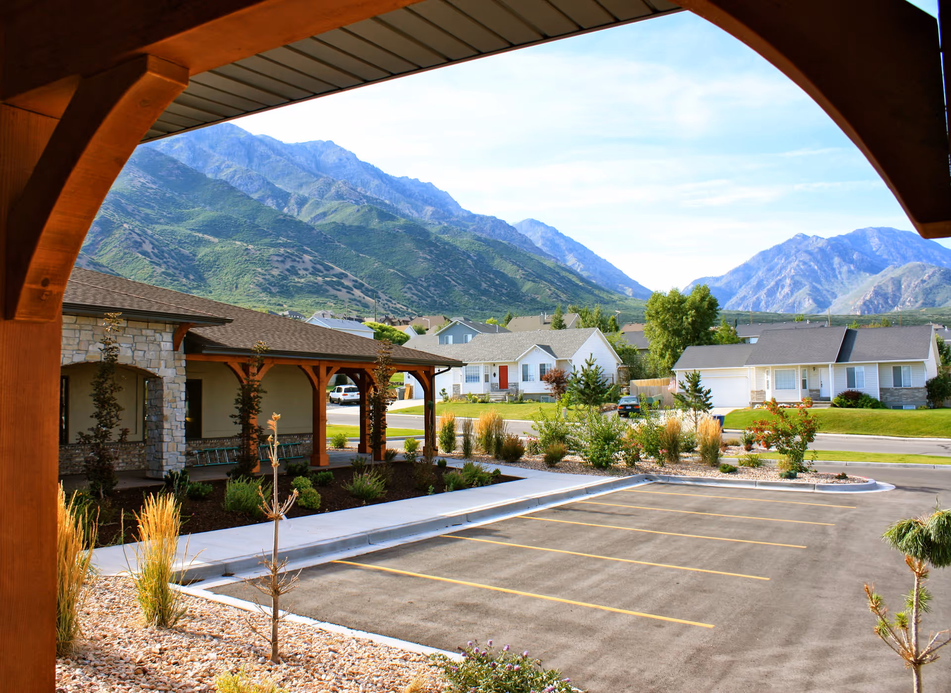 View from a covered entry over a parking lot and landscaped courtyard toward homes and mountains in the distance.
