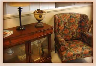 A floral upholstered armchair beside a wooden cabinet with a lamp in a cozy living room.