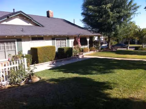 Front exterior of a single-story senior living home with a green lawn and shrubs