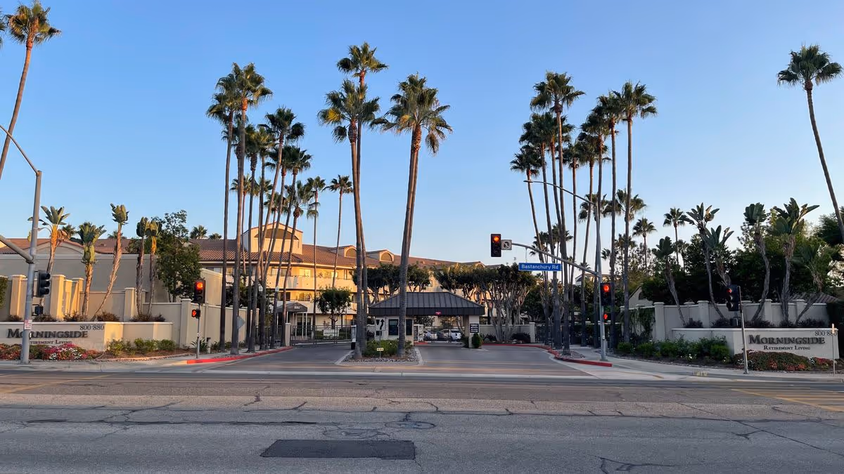 Entrance and front facade of Morningside of Fullerton senior living facility flanked by tall palm trees.