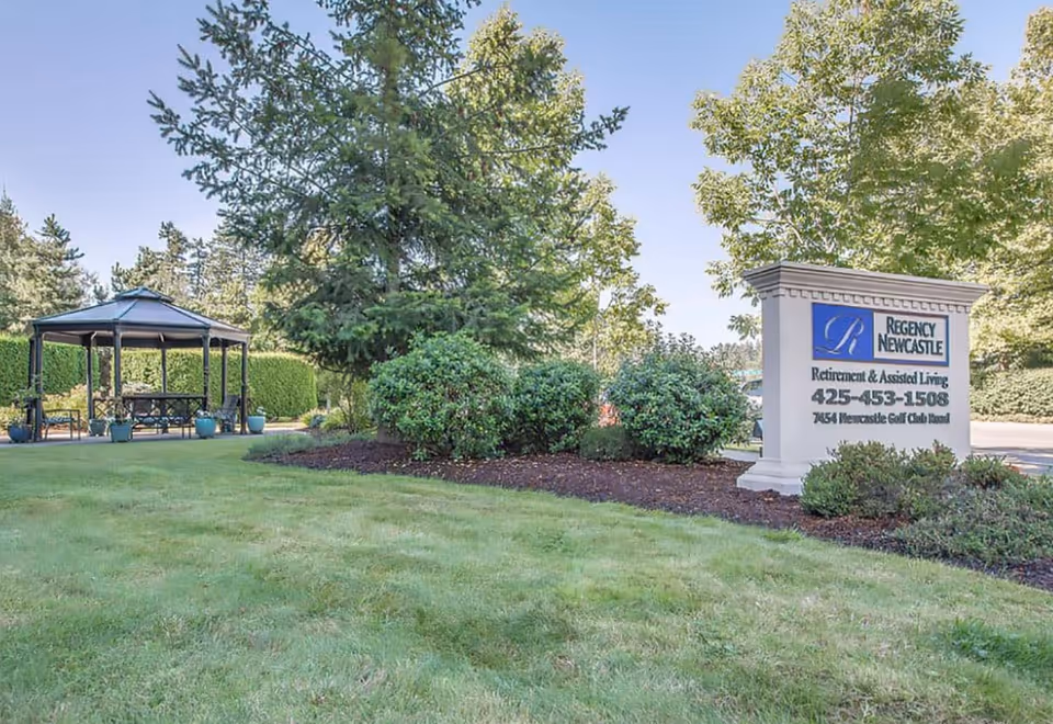 Entrance sign for Regency Newcastle on a landscaped lawn with a gazebo and trees in the background.