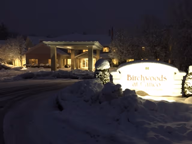Nighttime exterior view of Birchwoods at Canco Senior Living facility entrance with snow-covered ground and illuminated sign displaying the facility name.