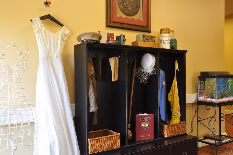 Interior entry area with a black cubby storage holding hats, coats and baskets, a white wedding dress hanging on the left, and a fish tank on the right.