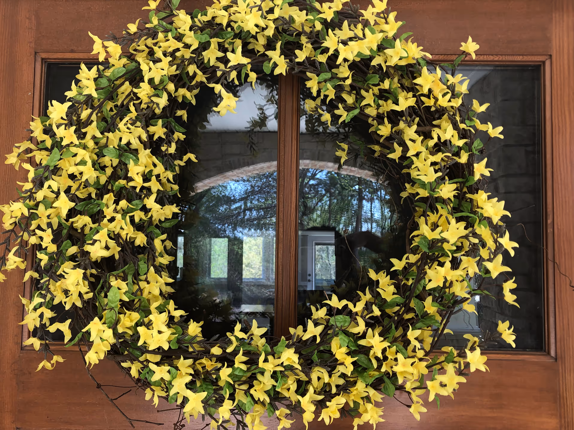 Wooden front door with glass panes decorated by a large wreath of yellow flowers.