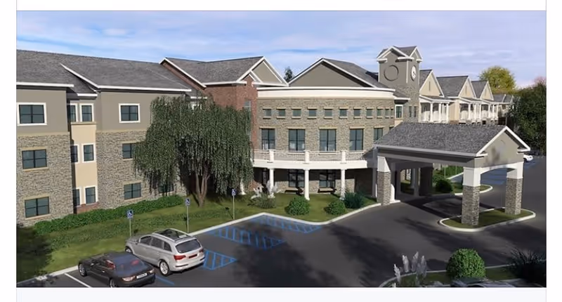 Exterior front view of a multi-story senior living facility with a covered porte-cochere, clock tower feature, parking spaces, and landscaped grounds.