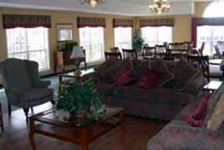 Communal lounge area with sofas, armchairs, a coffee table, and dining tables near large windows.