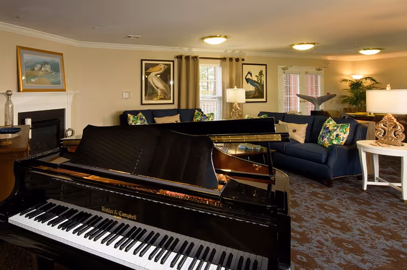 Spacious lounge with a grand piano in the foreground, blue sofas, artwork, and lamps.