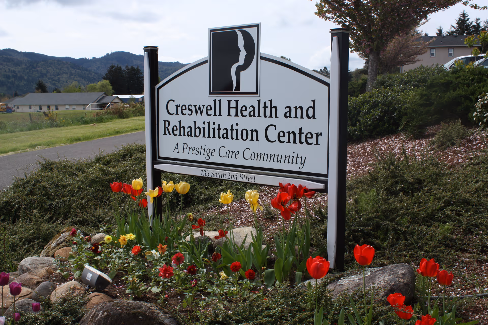 A landscaped entrance sign reading "Creswell Health and Rehabilitation Center" surrounded by tulips and shrubs with hills in the background.