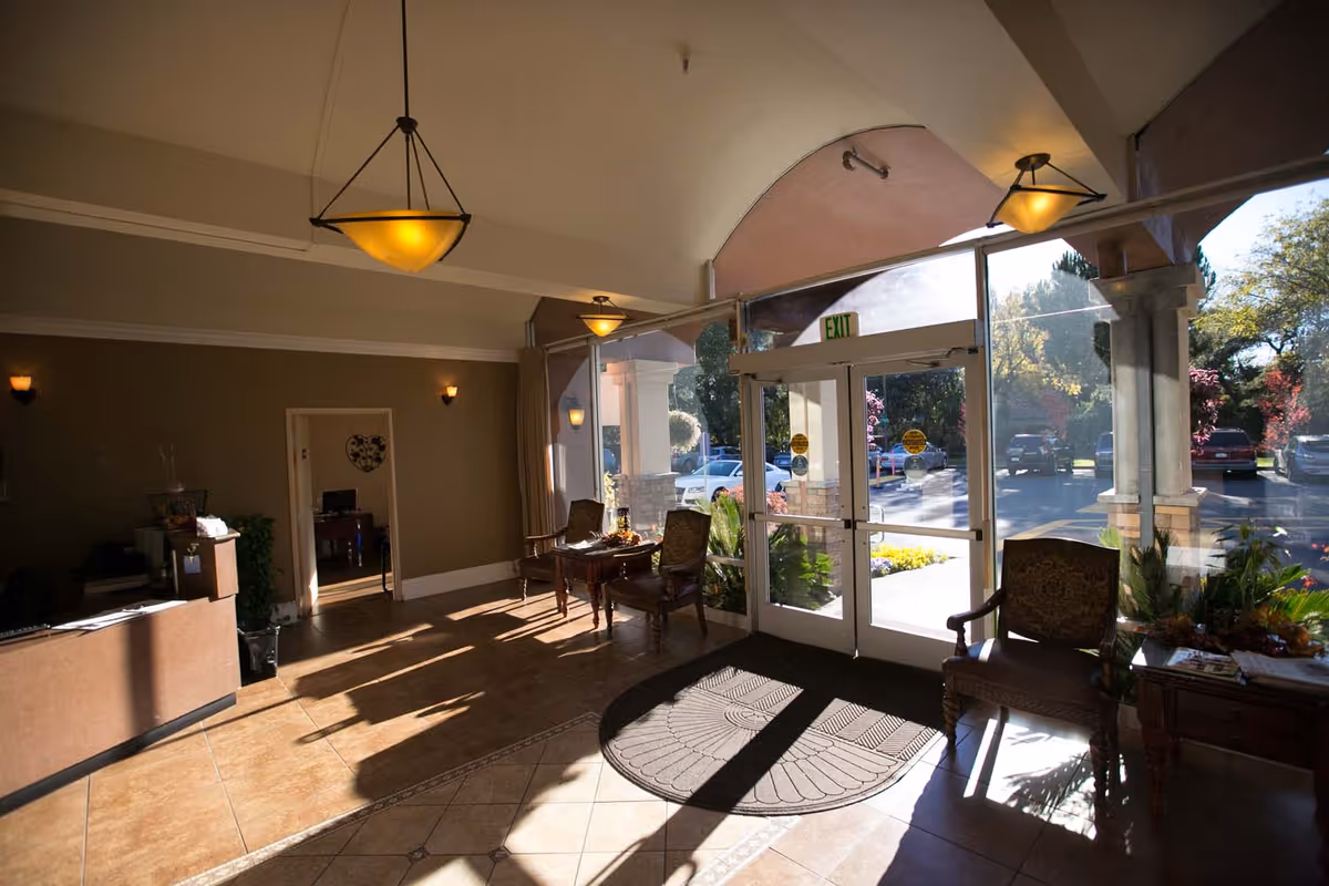 Sunlit entry lobby with glass double doors, chairs, small tables, and hanging pendant lights.