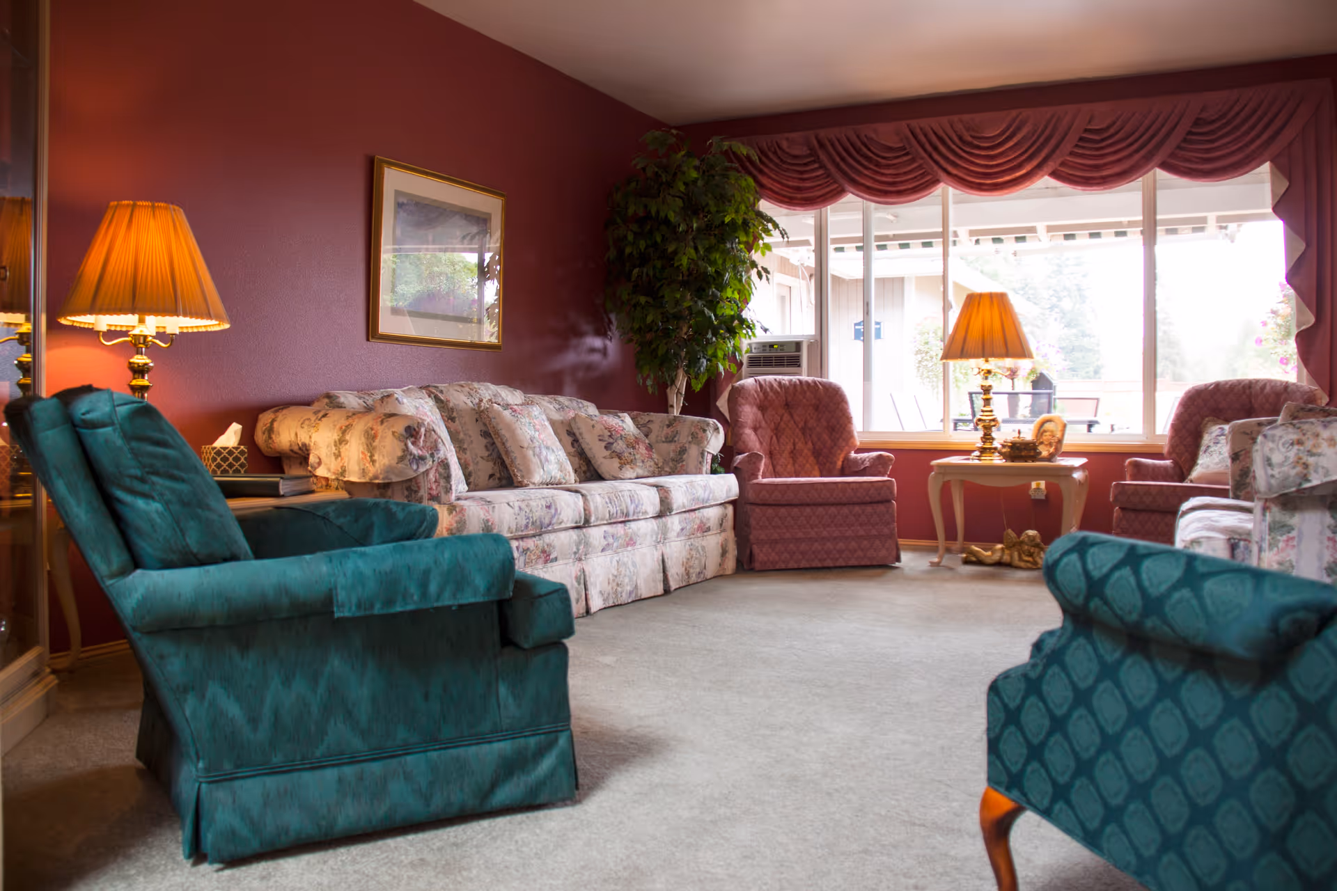 Cozy living room with floral sofa, upholstered armchairs, table lamps, and a large window.
