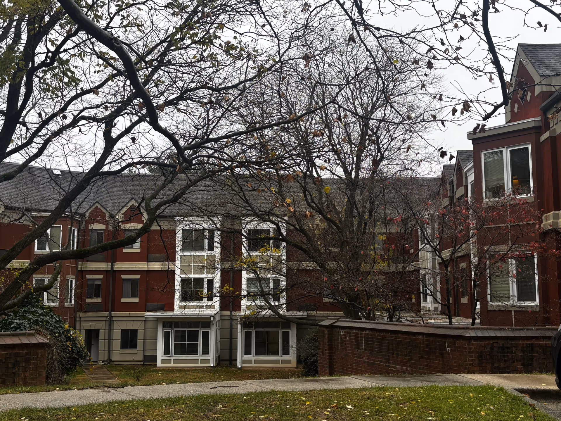 Front view of a red brick multi-story senior living building with bare trees and a small lawn.