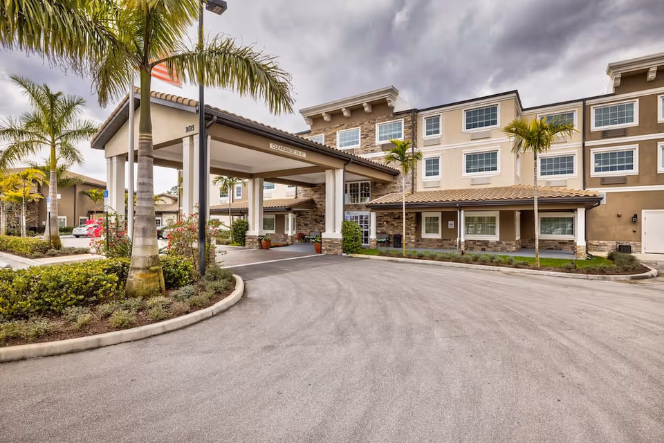 Entrance and porte-cochère of a multi-story senior living building with palm trees and a landscaped driveway.
