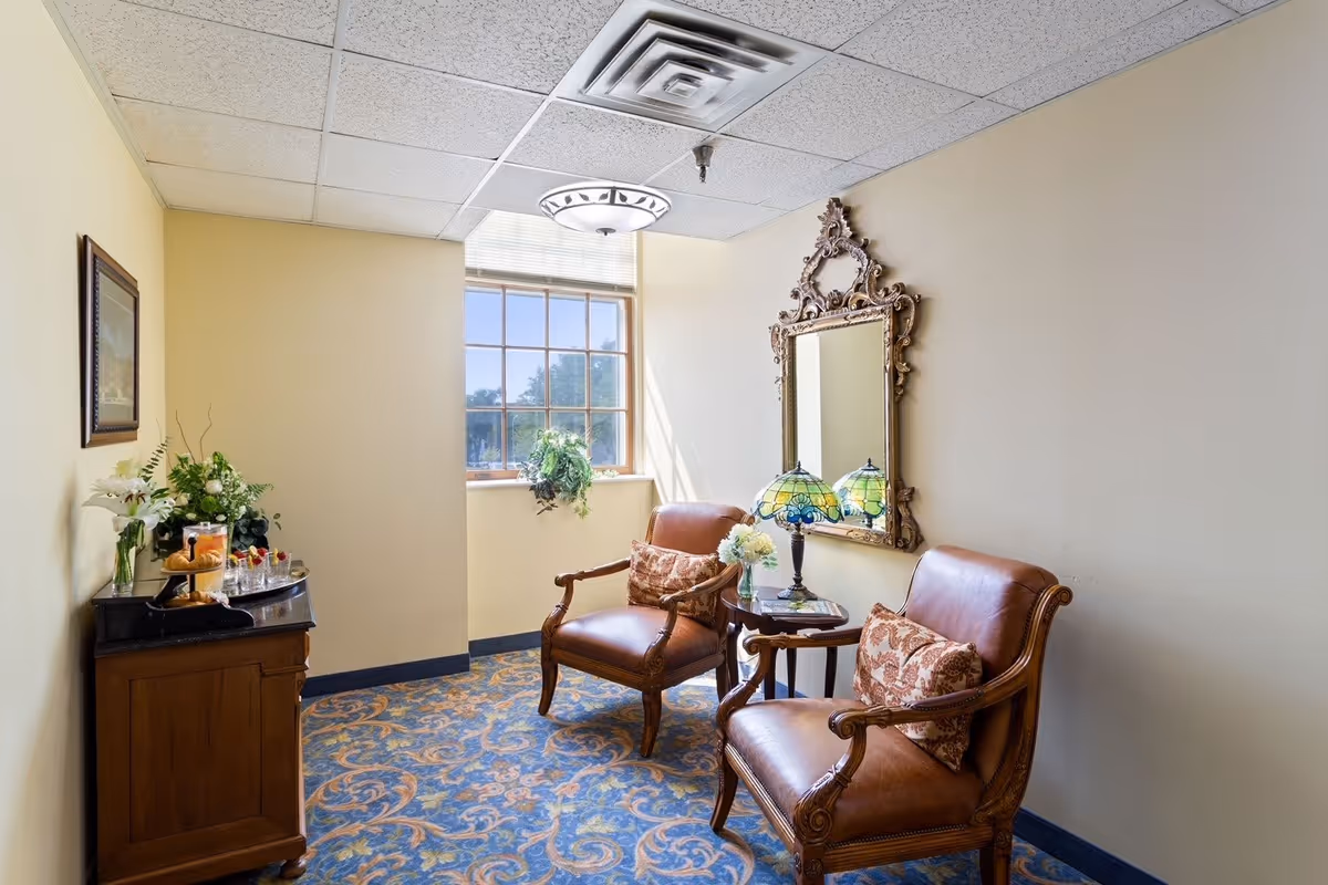 Small sitting area with two leather armchairs, a side table with a lamp and a decorative mirror beside a window.