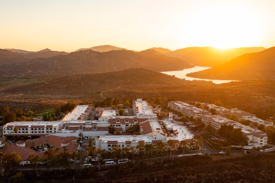 Aerial view of Casa de las Campanas senior living facility at sunset, surrounded by hills and a winding river in the background.