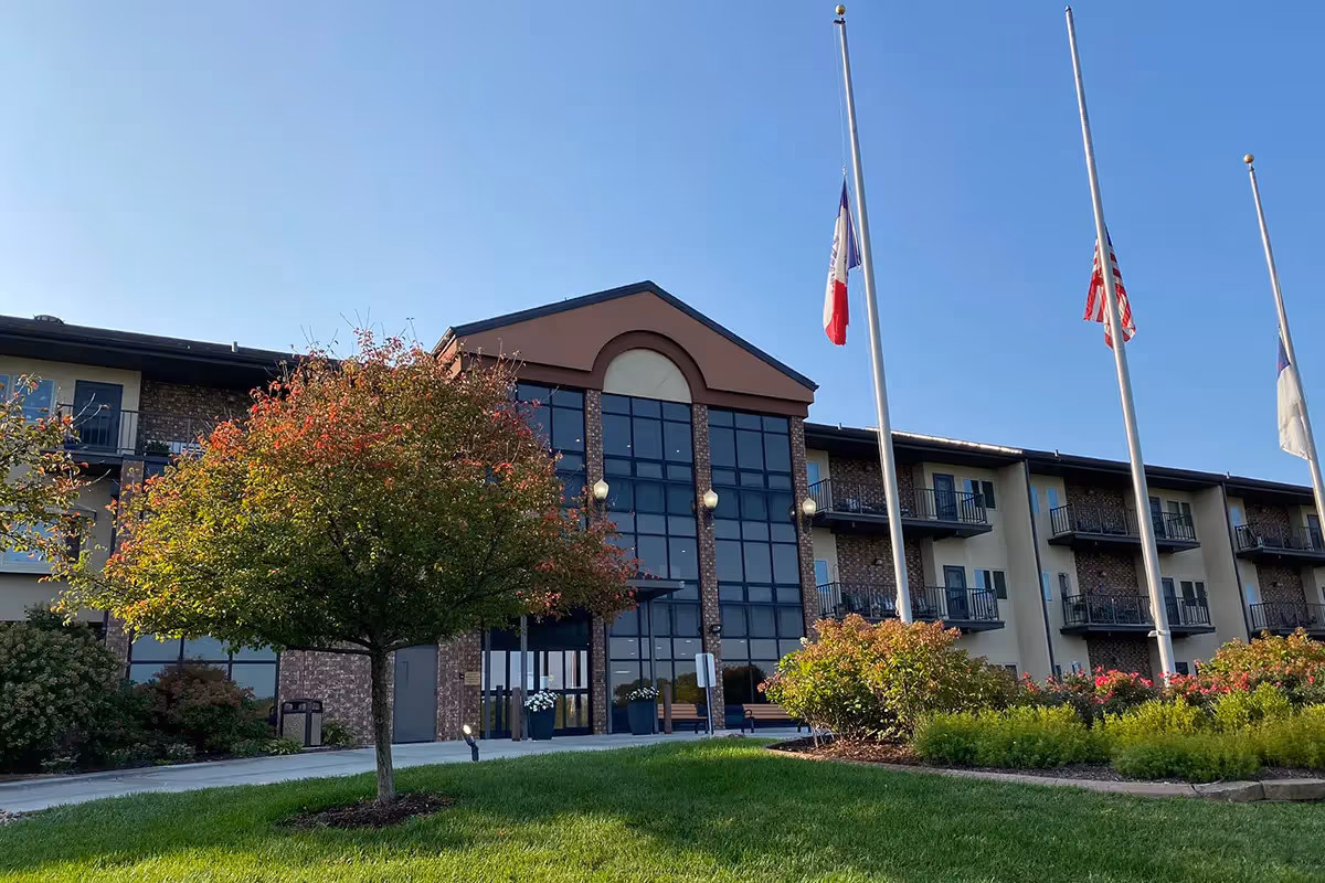 Exterior front view of Chapters Living of Council Bluffs, a multi-story senior living building with a glass entry and flagpoles.