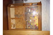 A wooden display cabinet with glass doors containing a decorative tree branch adorned with colorful bird figurines inside, placed against a wall with a tiled floor visible.