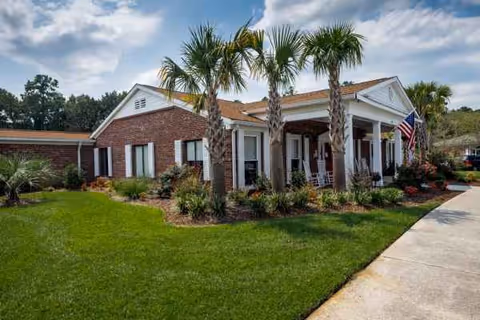 Front exterior of White Oak Manor Charleston featuring brick, palm trees, and an American flag
