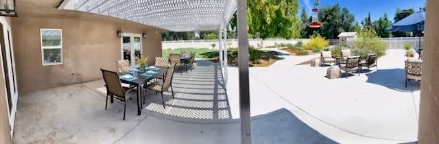 Outdoor patio area at The Hills of Stillman featuring a covered seating area with tables and chairs on the left side, and an open sunny space with additional seating and a fire pit on the right side, surrounded by greenery and trees.