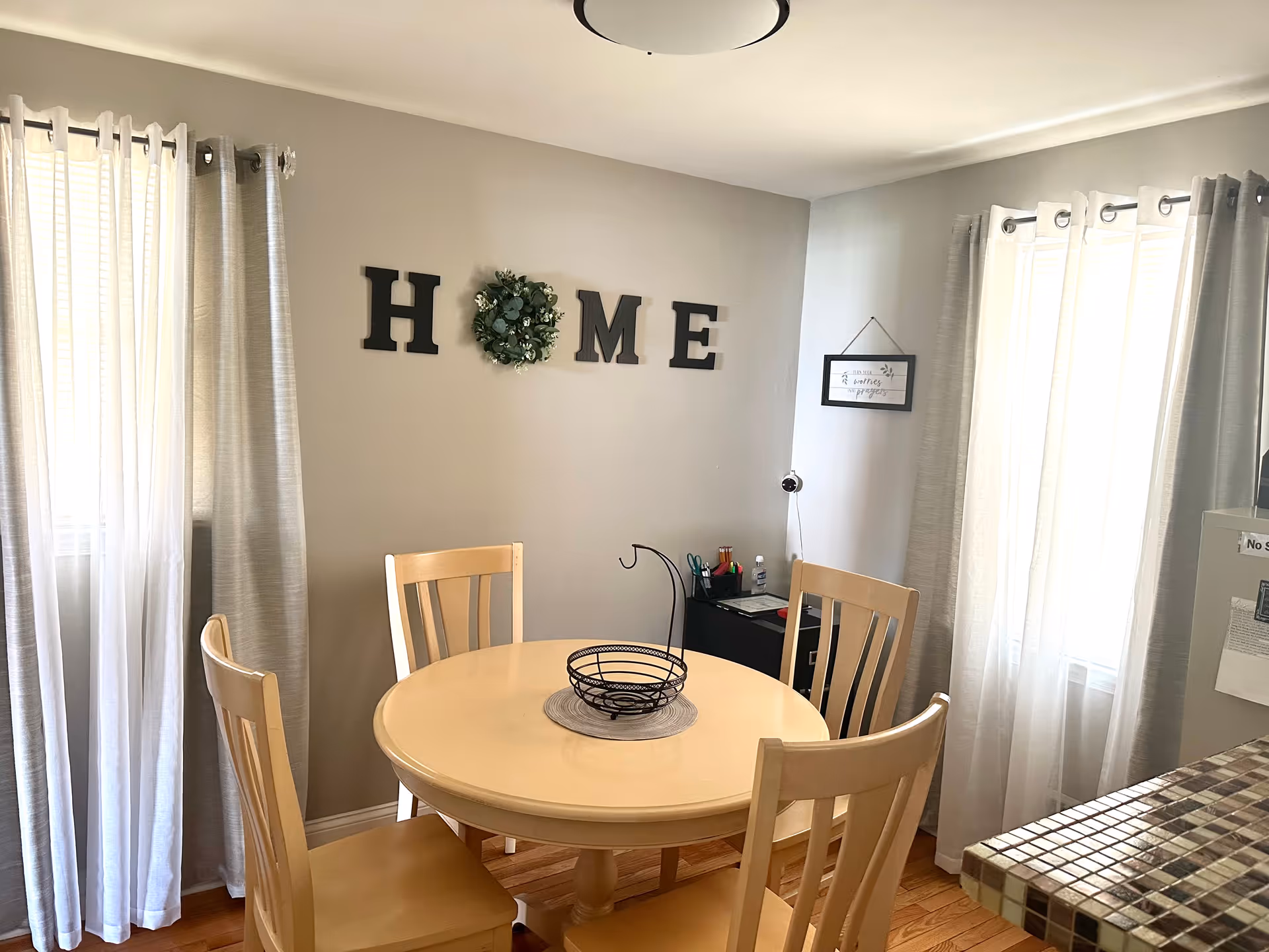 A cozy dining area with a round table, chairs, and light curtains in gray walls.