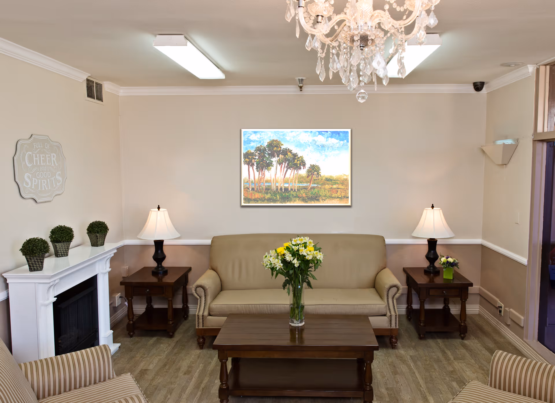 A cozy sitting area in a senior living facility with a couch, tables, and decorative plants.