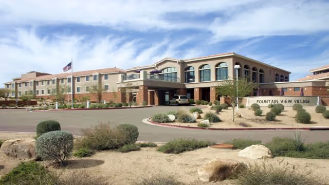 Exterior view of Fountain View Village with a circular driveway, signage, and desert landscaping.