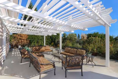 Outdoor seating area under a white pergola with cushioned chairs and tables.