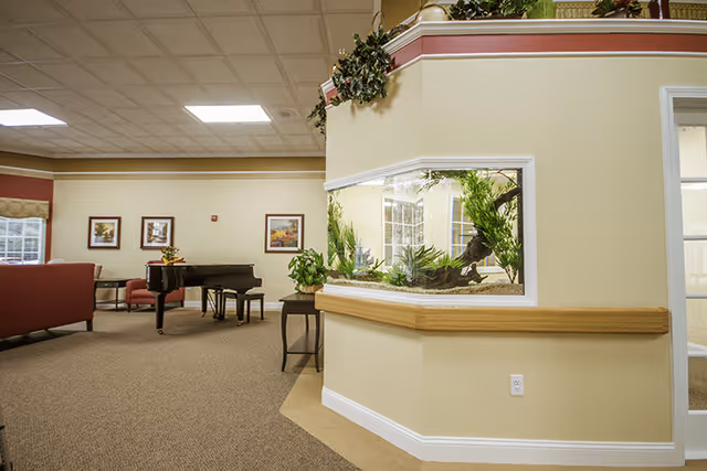A furnished common area with a built-in aquarium, piano, seating, and decorative plants.