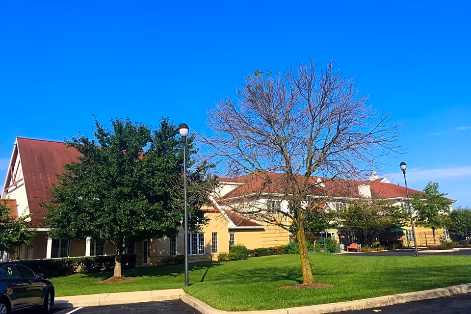 Creekside Village senior living facility exterior with red roof, trees, and a parking lot.