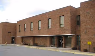 Brick two-story building with multiple windows and an entry area, John Manchin Sr Health Care Ct.