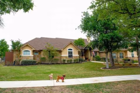 A single-story senior living facility with a manicured lawn and two small dogs on the sidewalk.
