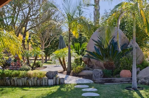 Landscaped outdoor courtyard with palm trees, a stepping-stone path, large boulders and seating areas.