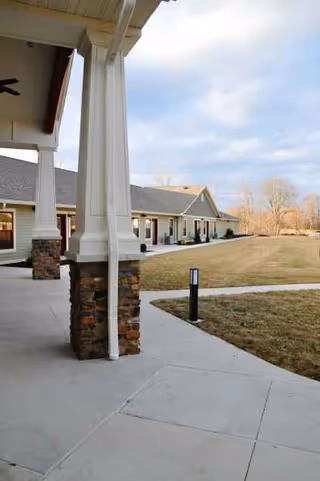 Exterior view of Stillwater Senior Living facility showing a covered porch, stone columns, and a lawn.