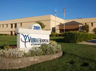 Exterior view of Vibra Hospital sign and front of beige building with landscaping.