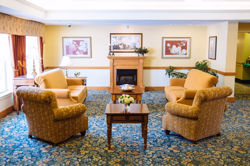 Cozy communal sitting room with upholstered armchairs arranged around a coffee table facing a fireplace.