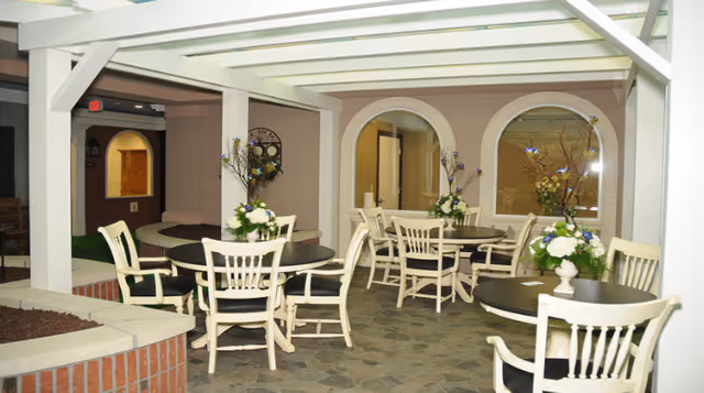 Indoor communal dining area with round tables, white chairs, floral centerpieces, and a pergola-style ceiling.