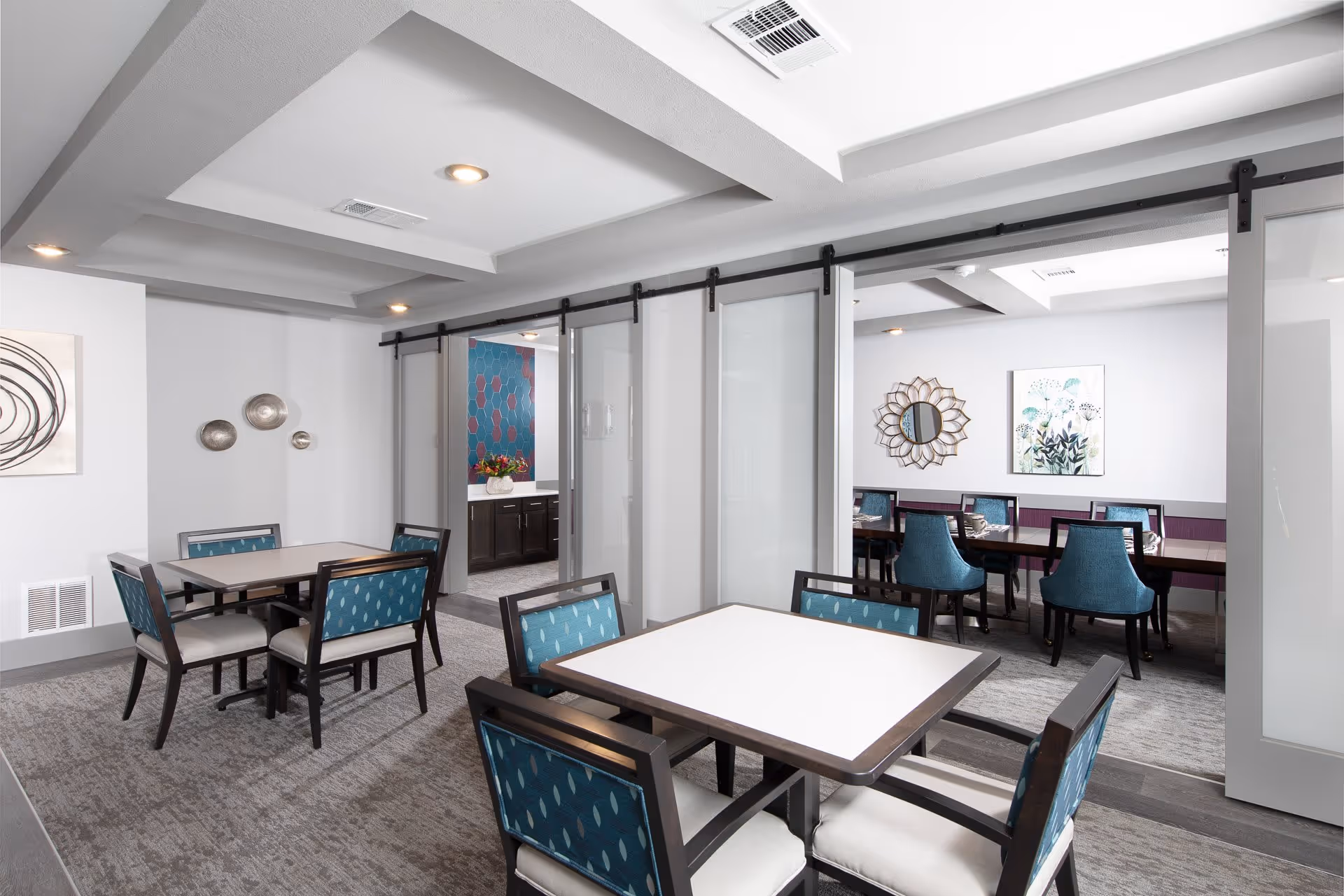 Bright modern dining room with several square tables and teal-upholstered chairs separated by sliding glass panels.