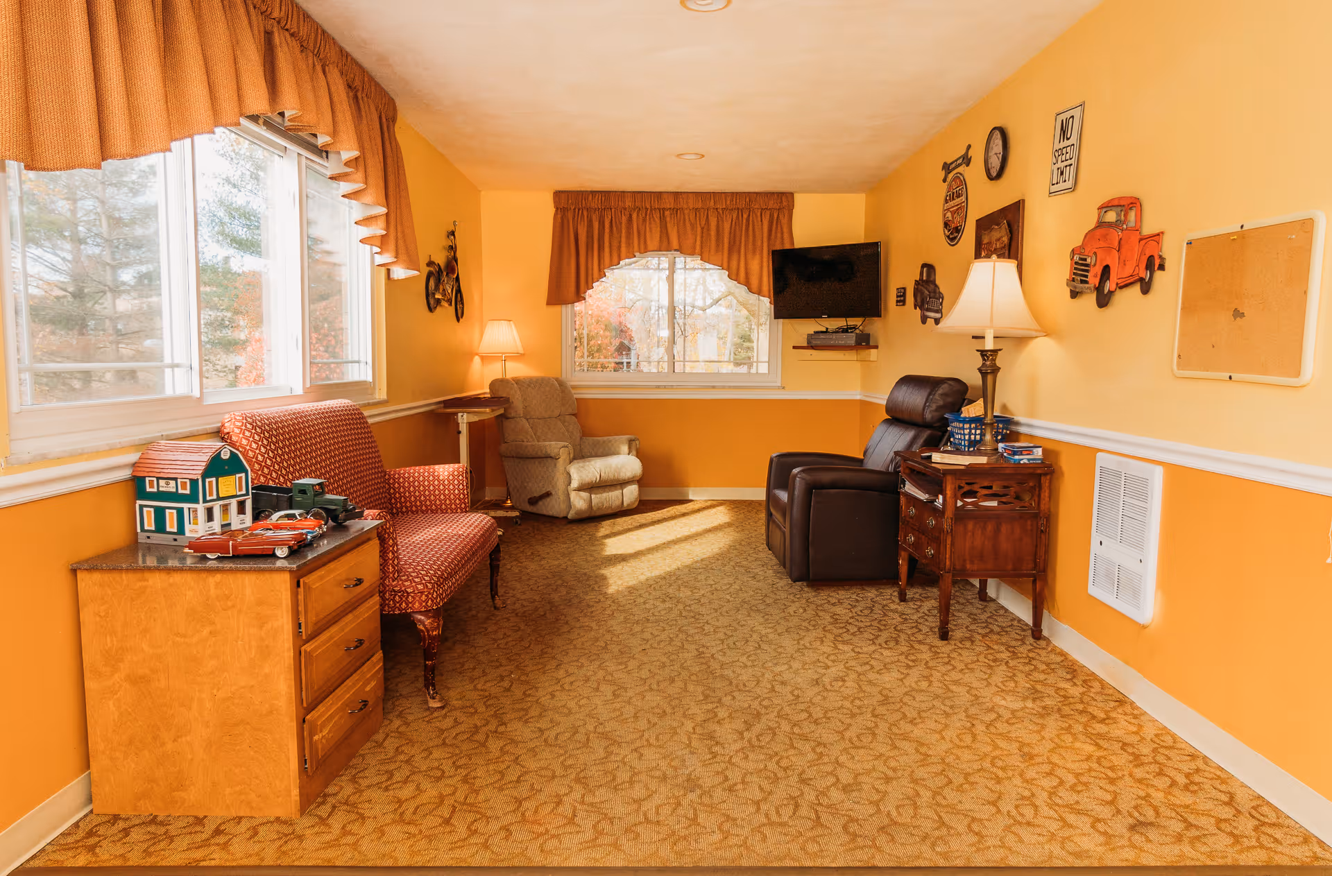 Cozy seating area in a senior living facility with armchairs, side tables, a wall-mounted TV, and decorative wall art.