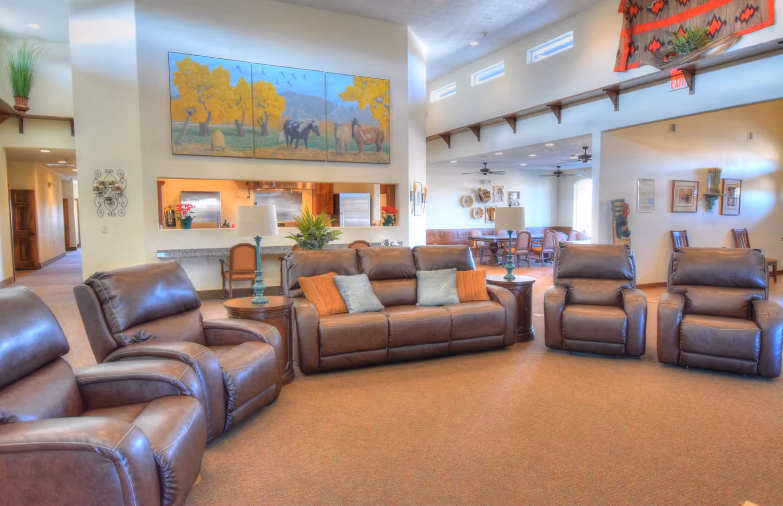 Spacious communal living room with brown leather sofas and recliners, side tables, and artwork on the wall.