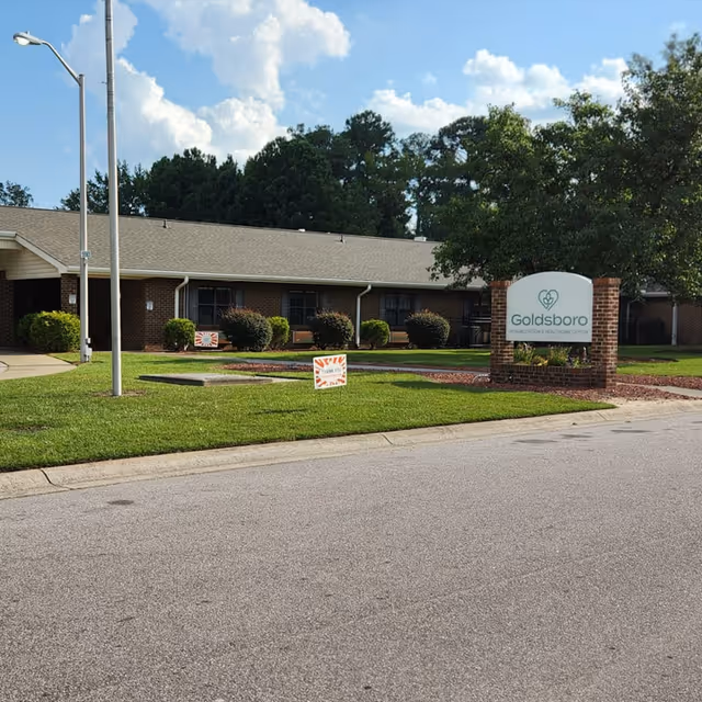 Front exterior of a single-story brick rehabilitation and healthcare center with a lawn, shrubs, and a sign reading Goldsboro.