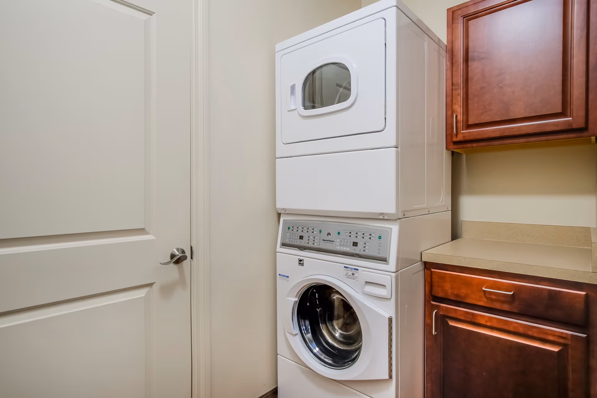 A stacked washer and dryer next to wooden cabinets and a countertop in a small laundry room.